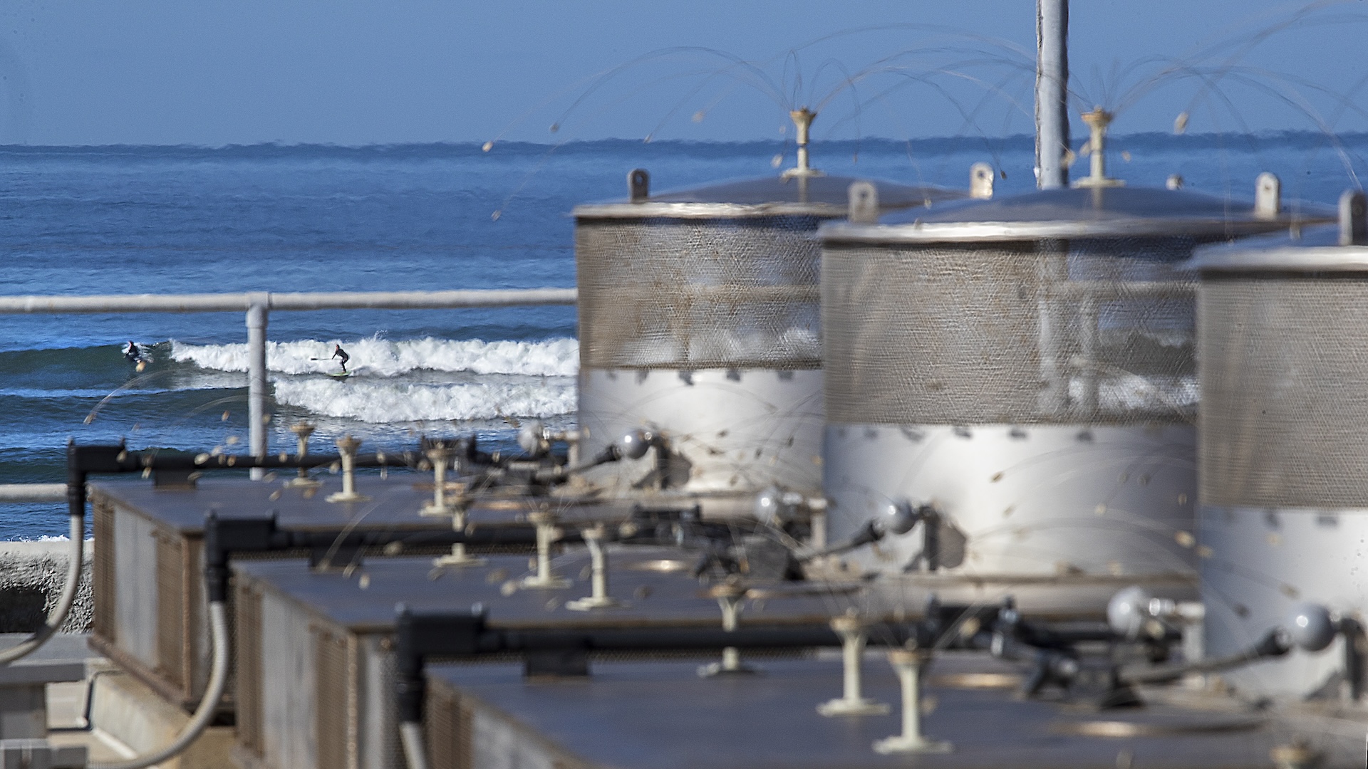 A view of the dry spent fuel storage facility in the foreground as surfers ride the waves at San Onofre State Beach