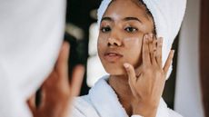Woman in a towel applying moisturiser to her face
