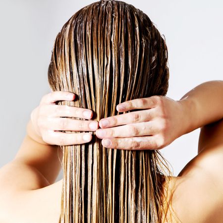 rear view of woman applying conditioner on hair against white background
