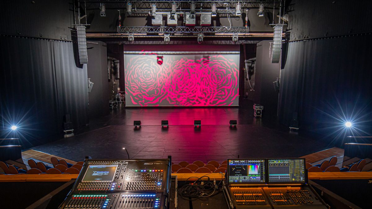 The stage at a Polish theater is lit with a pink backdrop and surround by Meyer Sound audio solutions. 