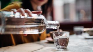 Woman's hands pouring a glass bottle of water into a glass