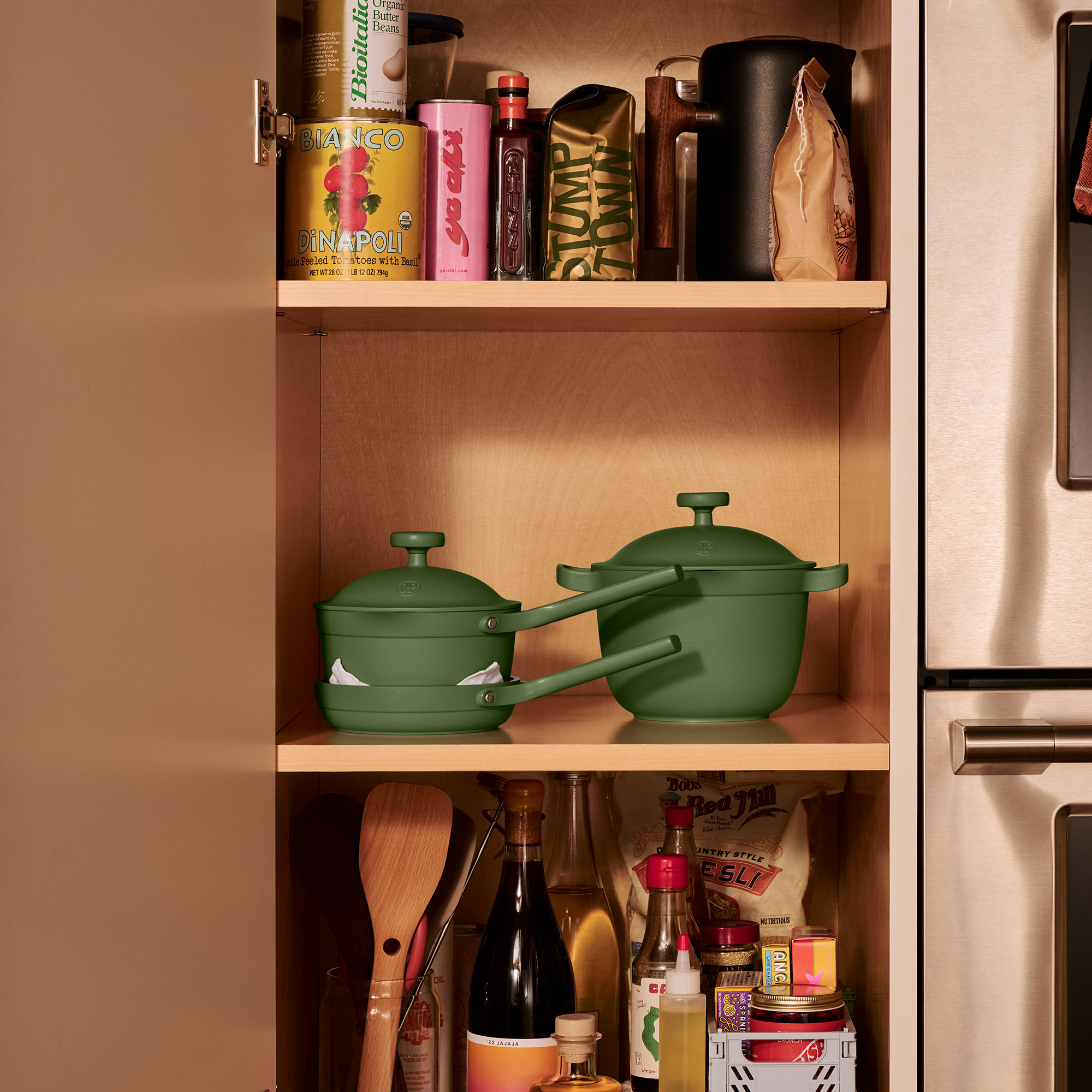 Three green mini Our Place cookware items on kitchen cupboard shelf