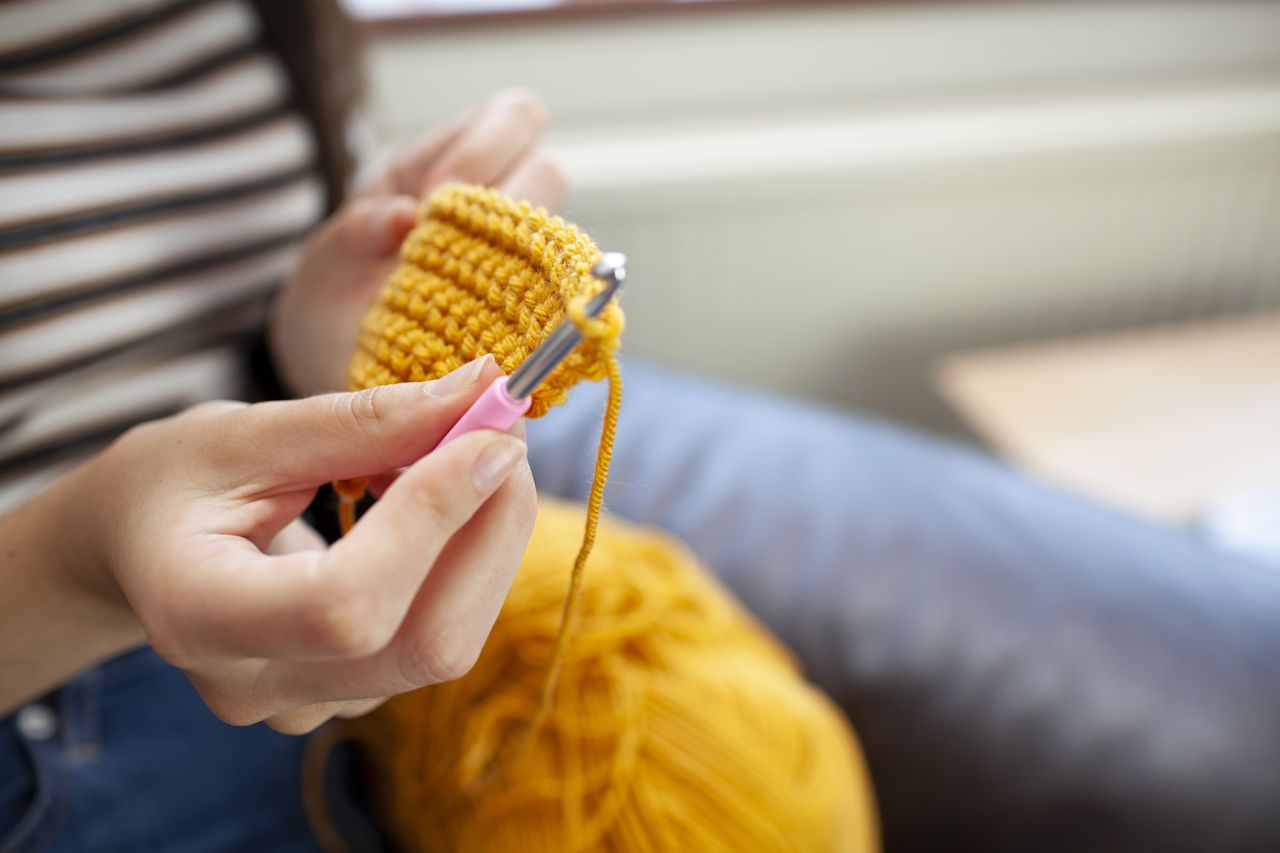 A woman crochets an item using bright yellow yarn