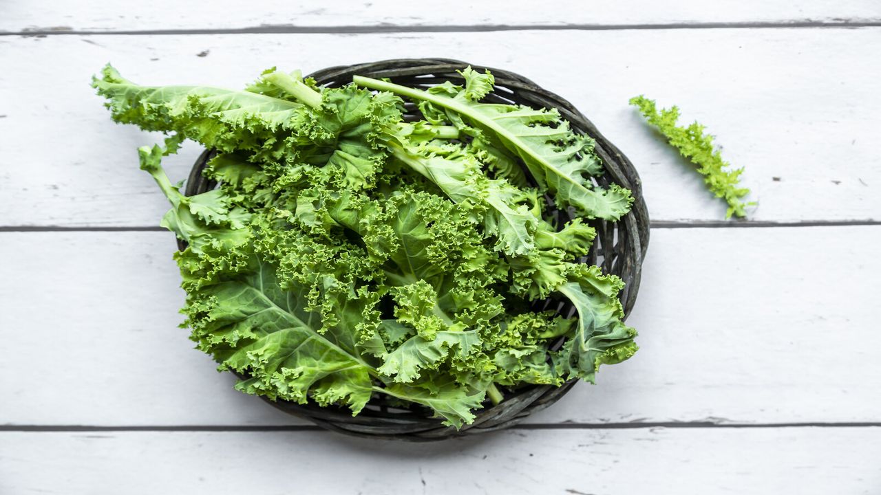 kale in a wicker basket on a white wooden floor