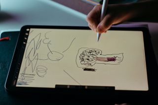A close up of a child's hand as they use a stylus to draw on a tablet