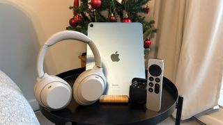 An iPad, Sony headphones, Bose earbuds and an Apple TV remote in front of a Christmas tree