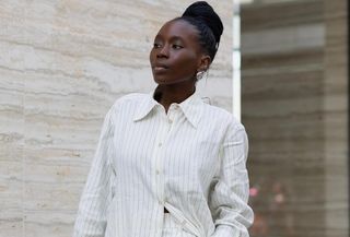 a photo of one of the best shirtdress outfit ideas with a woman wearing a white striped maxi over matching trousers with silver shell earrings