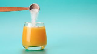 spoon of collagen powder being mixed into a glass of orange juice