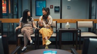 From left to right: Awkwafina and Sandra Oh sitting togehter at a hospital. Sandra Oh is holding her seemingly broken wrist.