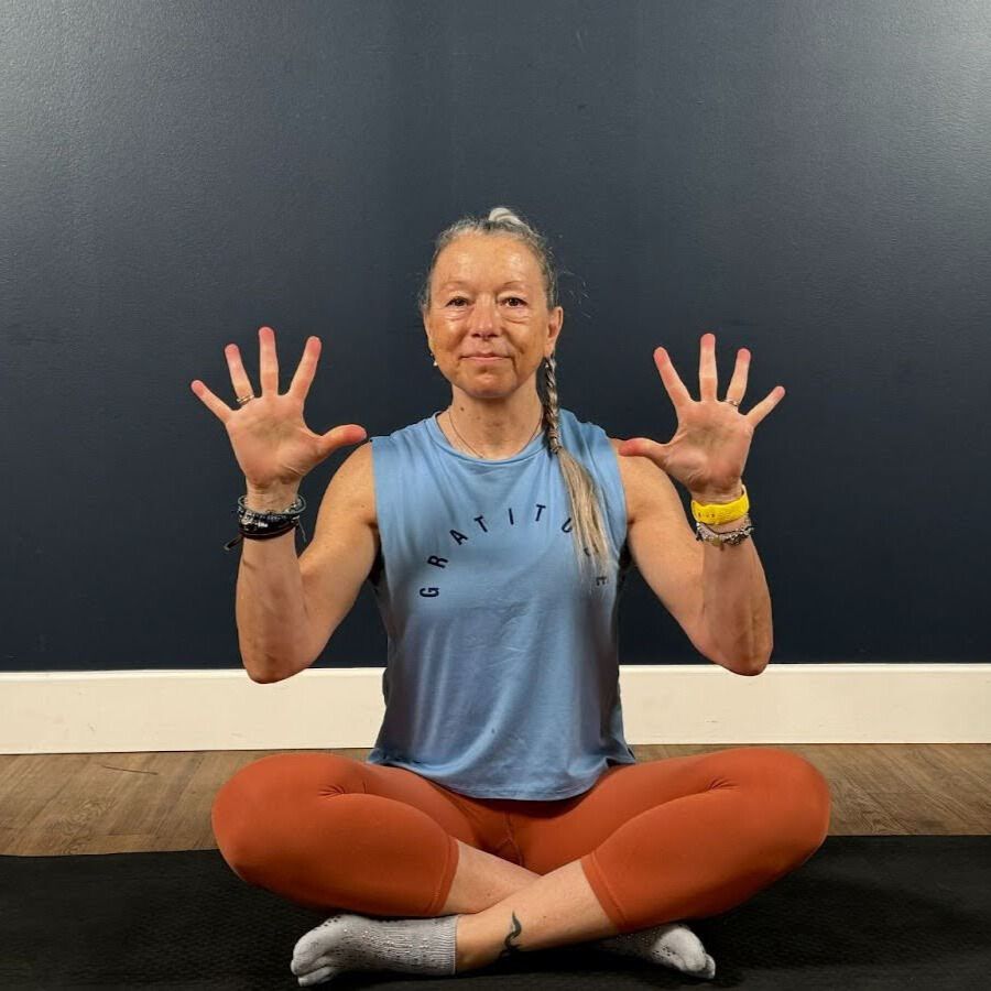 Woman sits cross-legged on mat demonstrating wrist movement
