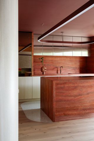 A red/orange marbled counter and back splash with blond wood flooring