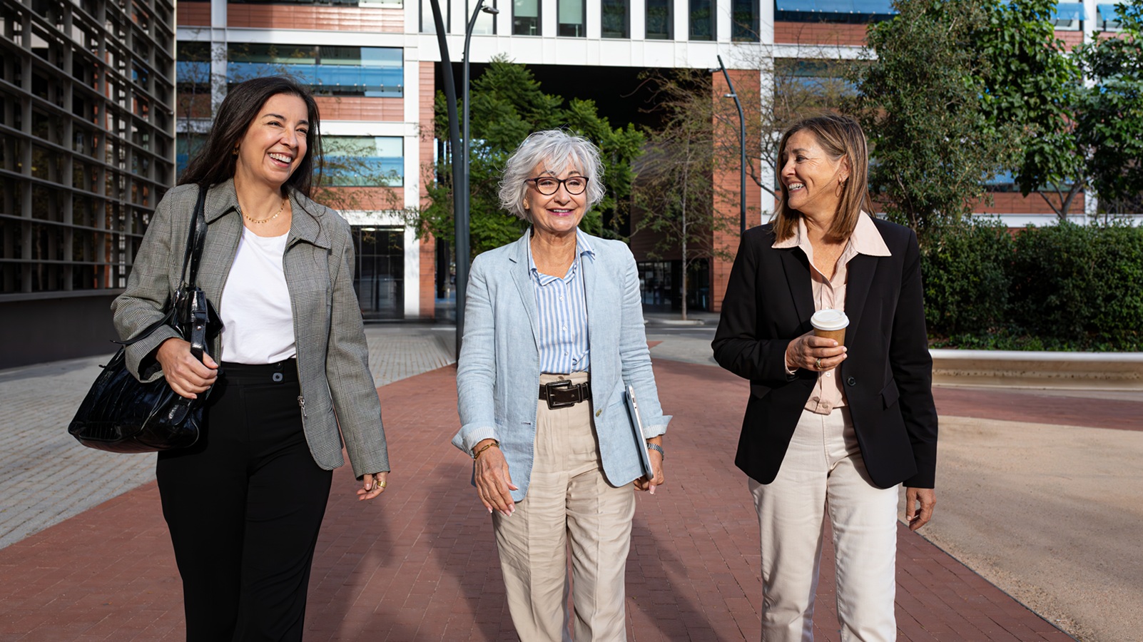 Three smiling businesswomen are walking and talking together outside of their office building during their work break