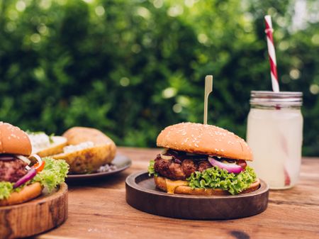 Cheeseburgers with a beverage outdoors on a wooden table in a backyard