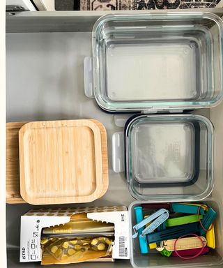 Rectangular and square glass food containers next to bamboo lids, plastic food bags, and plastic food clips in a kitchen drawer.