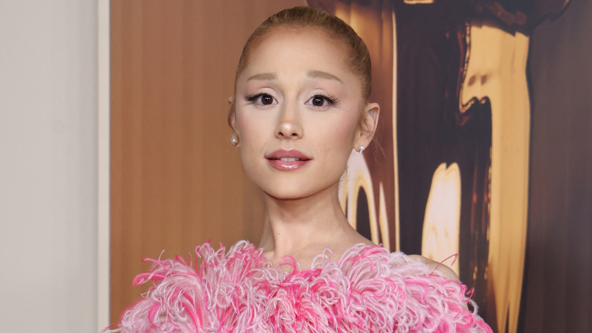 Ariana Grande wearing a slicked back ponytail as well as a black dress that has pink and white feathers at the neck line. 