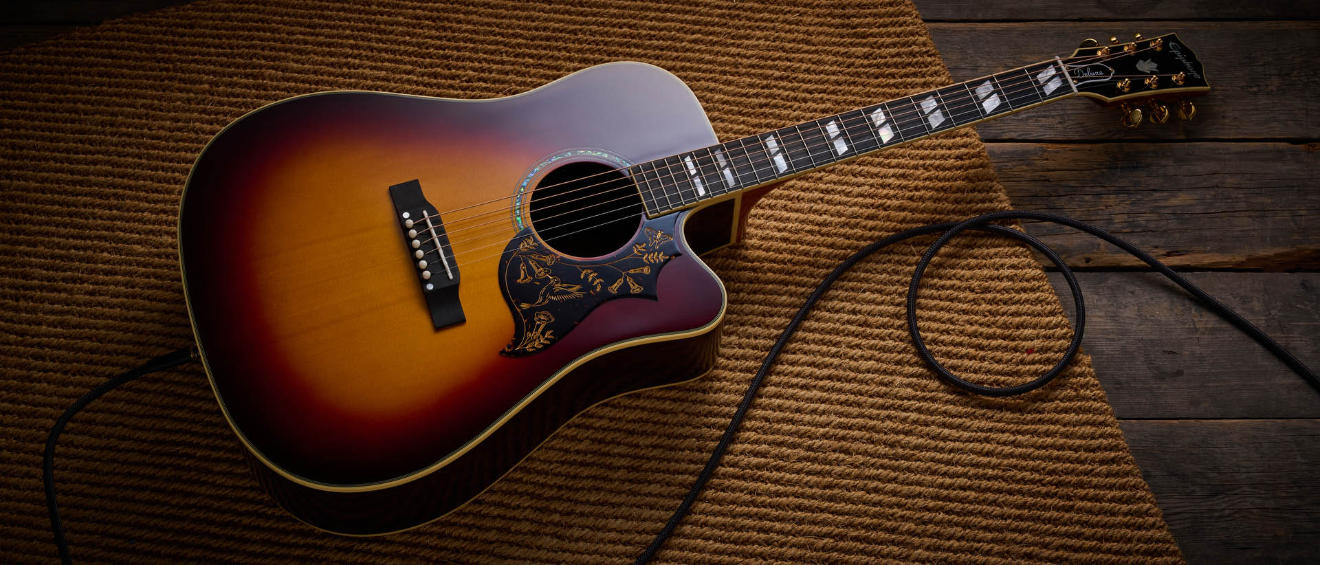The Epiphone Inspired by Gibson Custom Hummingbird photographed in all its glory, in close-up and against a wheat-coloured rug.