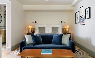A room in the Redchurch Townhouse hotel. The large, pale green bed is covered in white linen with a deep blue couch and a wooden table in front of it. The walls are painted in light cream color and there are 4 pictures handing on the wall.