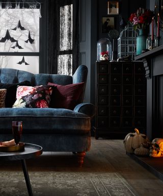 decorating with pumpkin ideas, dark and dramatic living with pumpkins in fireplace, webs and bats at window, gothic feel, birdcages, candles, indigo walls and couch, rug, berry cushions, antique sideboard