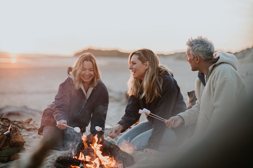 a group of adults roasting marshmellows around a campfire