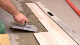 Hand laying tile adhesive on floor next to light wood effect floor tiles