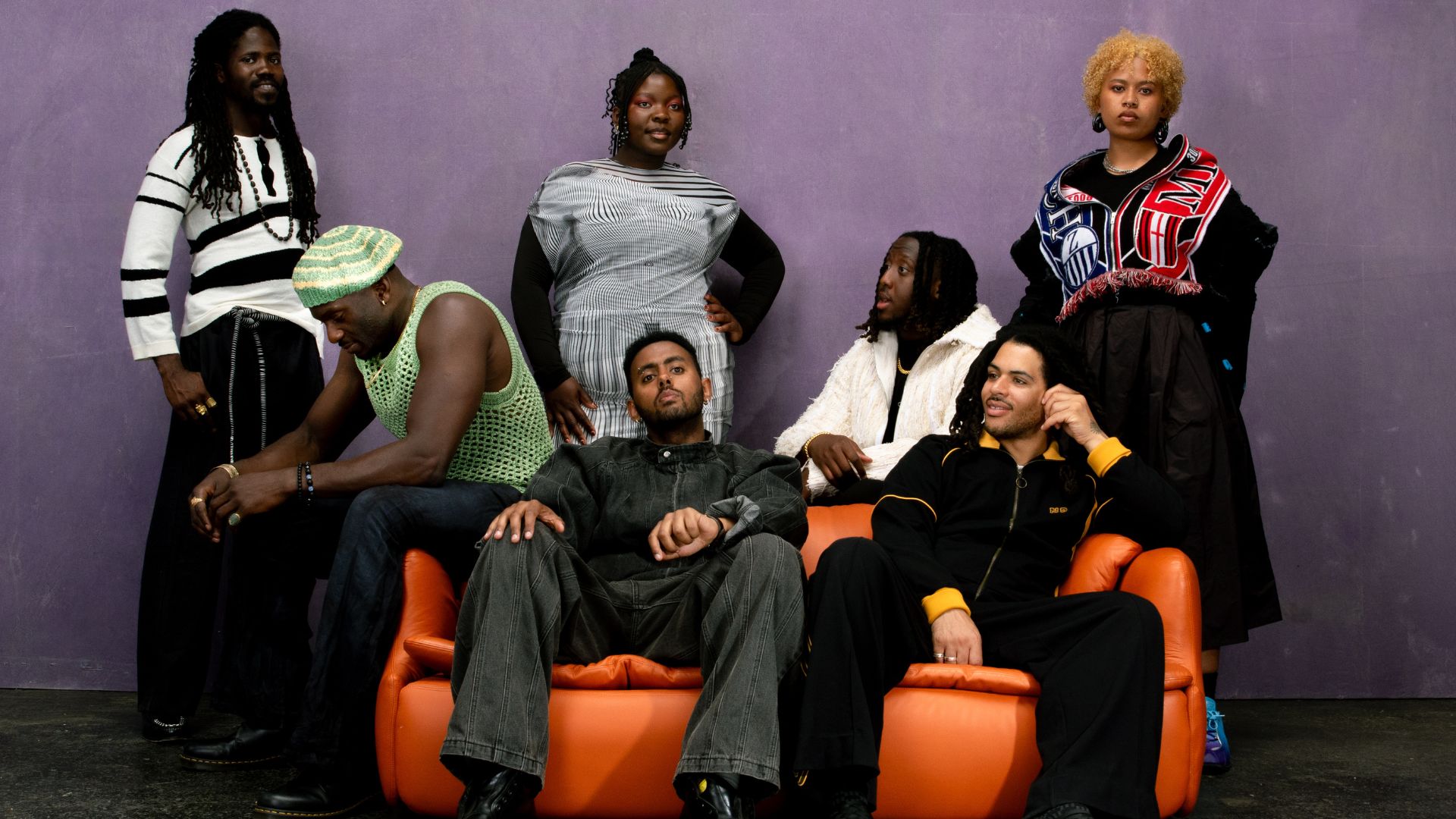 an image of the band kokoroko sitting on and behind an orange sofa