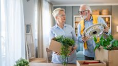 An older couple consult each other as they unpack their belongings in a house.