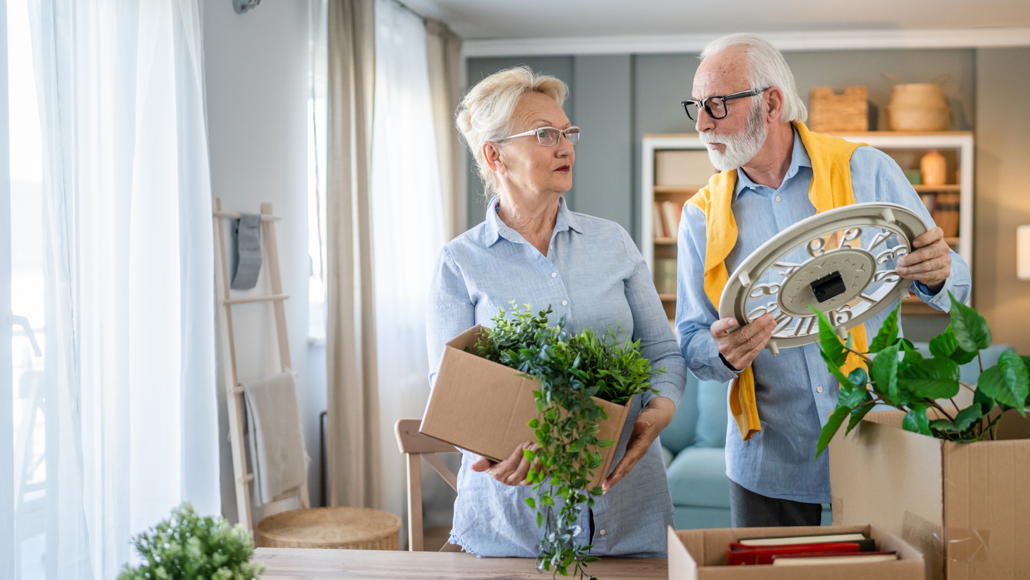 An older couple consult each other as they unpack their belongings in a house.
