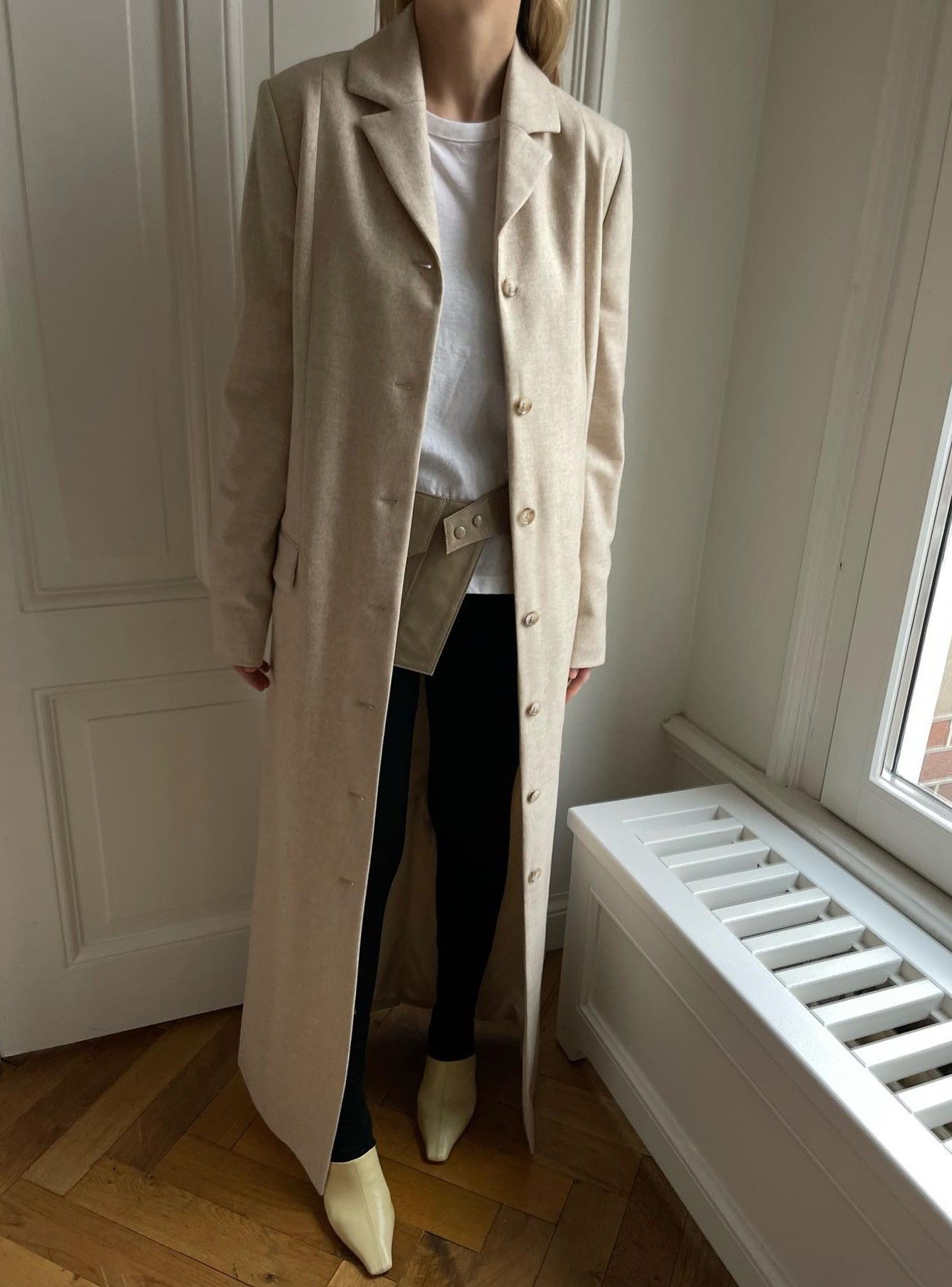 An image of @stephaniebroek wearing a cream trench coat with a white t-shirt, leggings, yellow square-toe flats and a belt.