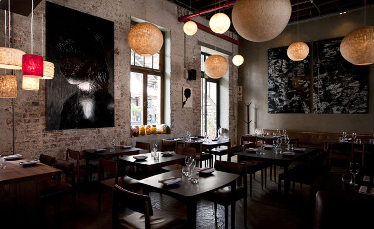 Black tables and chairs with rustic brick wall and exposed pipes with no ceiling