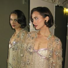 An image of actress Maude Apatow wearing a vintage bob hairstyle and looking at herself in the mirror.