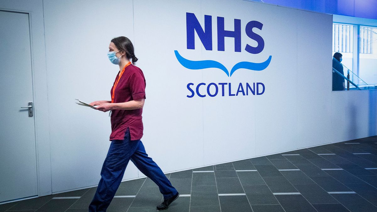 NHS Scotland sign pictured at a vaccination center in NHS Dumfries and Galloway with nurse in scrubs walking by.