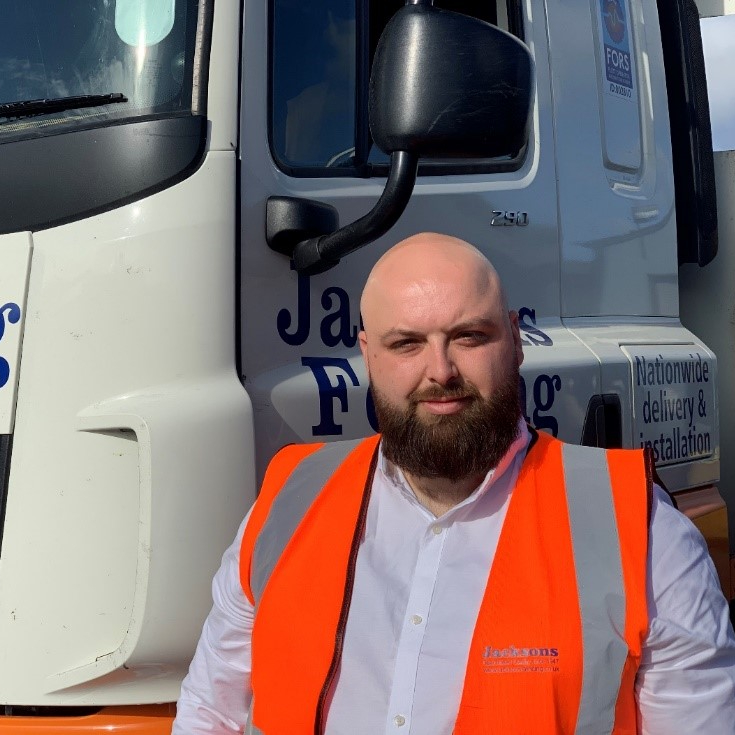 man with bald head, beard, wearing orange hi-vis jacket and white shirt in front of lorry cab