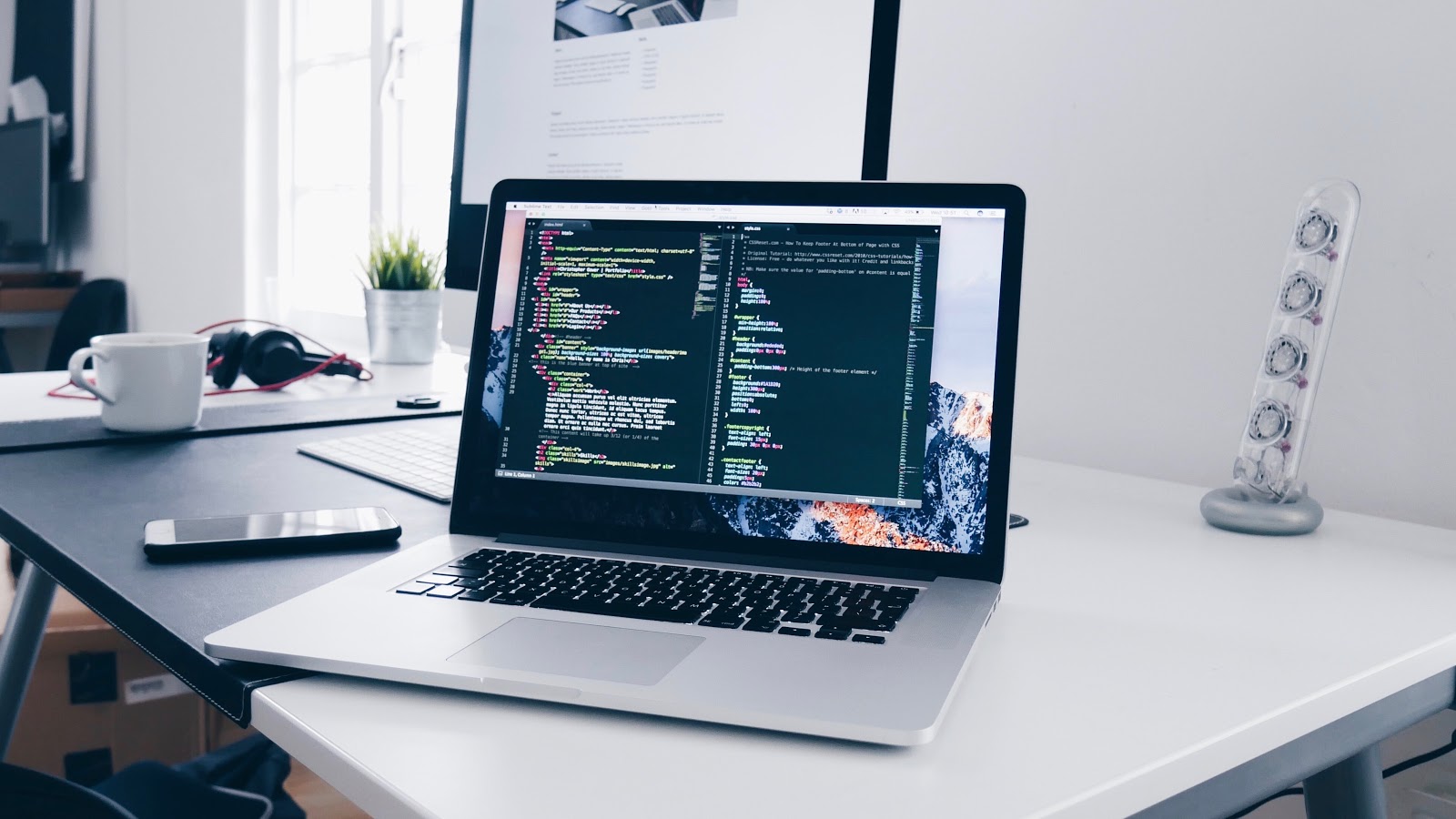 laptop on a desk by a monitor, with code displayed on the laptop screen