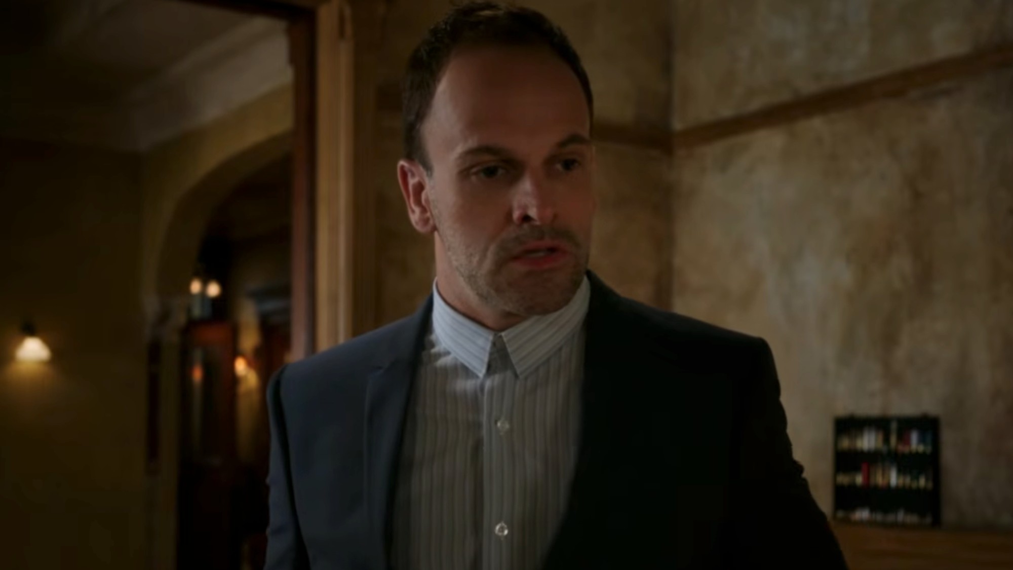 Jonny Lee Miller as Sherlock Holmes, wearing a striped shirt and looking very series in Elementary