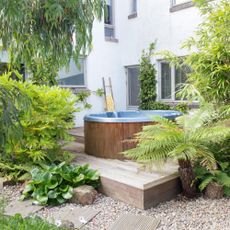 Gravel and decked area with a wooden hot tub surrounded by trees and ferns.