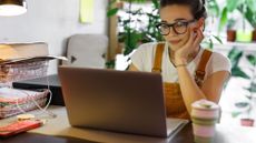 Young woman looking at an open laptop in front of her with office supplies on the desk around her