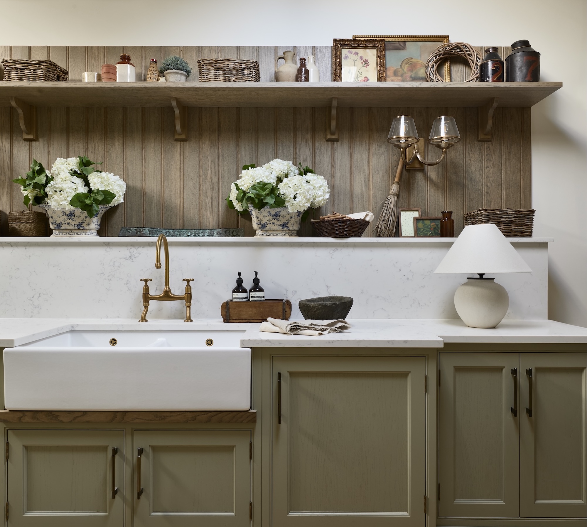 A modern traditional olive green kitchen with wall light and lamp, brass accents and black hardware