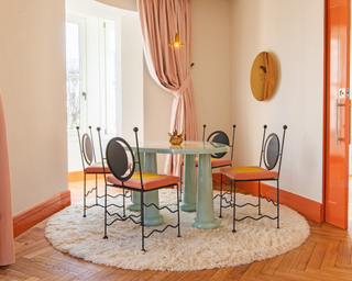 Brightly colored dining area with blue table, soft walls, orange accents and pink curtains.