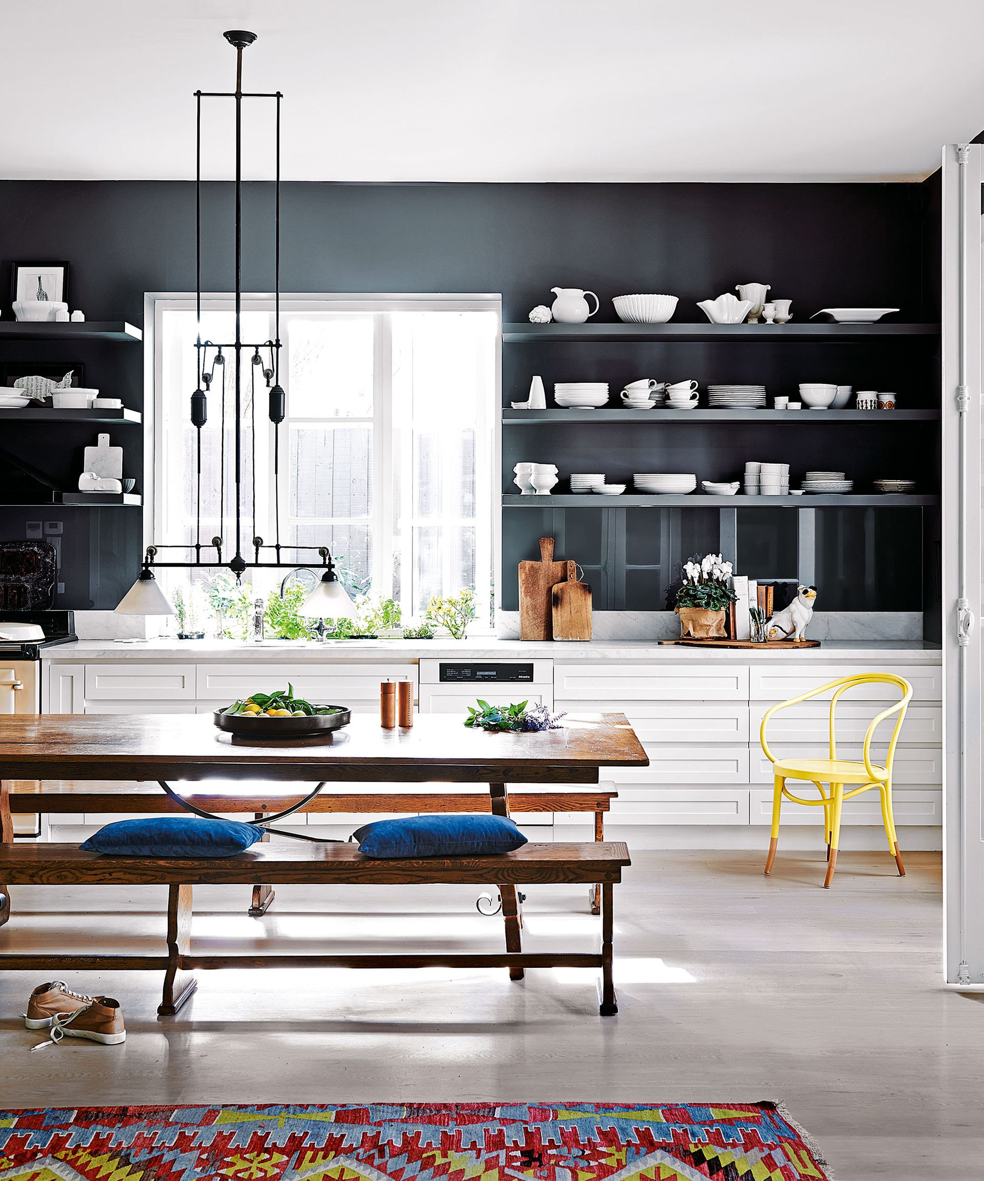 A large black and white kitchen with a wooden dining bench, open shelving storing crockery and a colorful rug