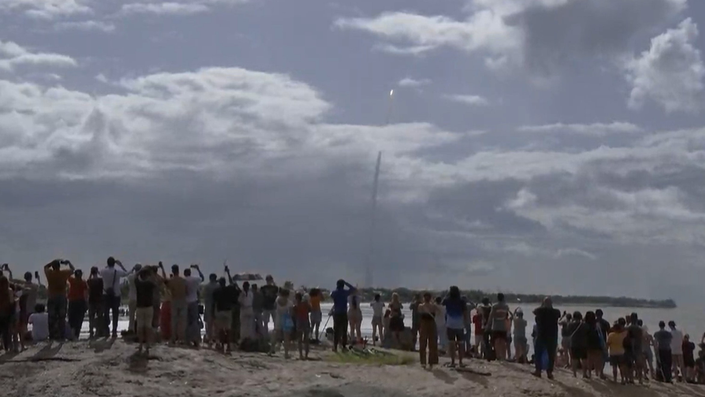 a large white rocket lifts off through a cloudy sky above a massive plume of fire and smoke