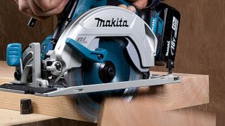 Blue Makita circular saw cutting through plank of wood with blurred offcut falling off
