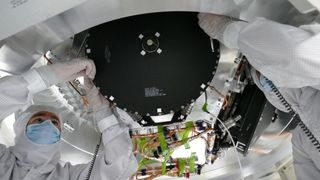 two masked people in protective suits work at the bottom of a spacecraft