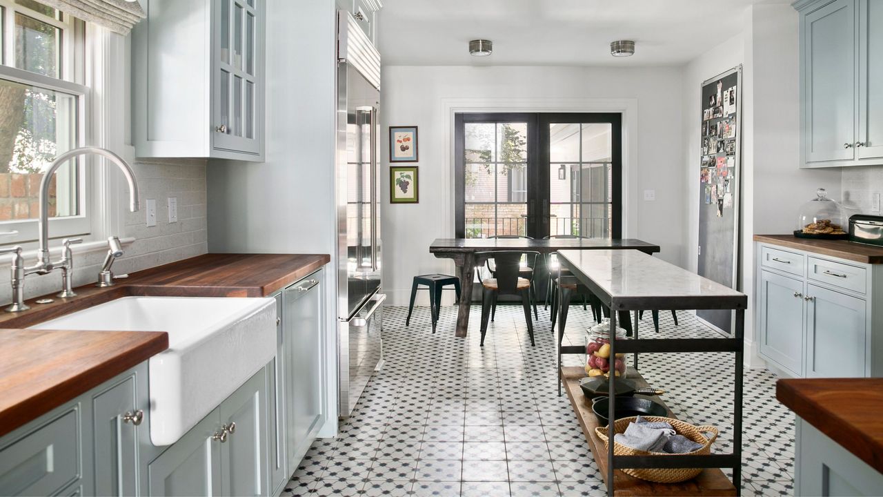 Small kitchen layout ideas are always useful. Here is a a white kitchen with blue cabinets, a black kitchen island, and black dining table and windows