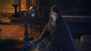 Elden Ring - Fia sits on a bed in the Round Table Hold wearing her black cloak and hood.