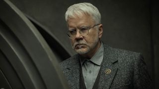 A stern-looking bearded man coming out of a vault door