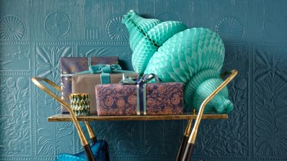 Blue textured wall with a gold drinks trolley in front of it loaded with gifts wrapped in gold and blue paper