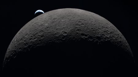 Earth sets at 6:41 p.m. EDT, April 6, 2026, over the Moon&rsquo;s curved limb in this photo captured by the Artemis 2 crew during their journey around the far side of the Moon. Orientale basin is perched on the edge of the visible lunar surface. 