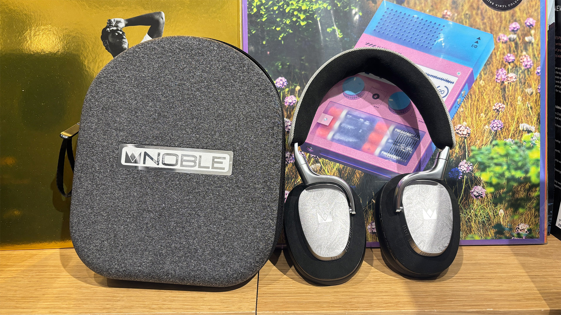 Noble Fokus Artemis over-ear headphones next to case on busy bookshelf
