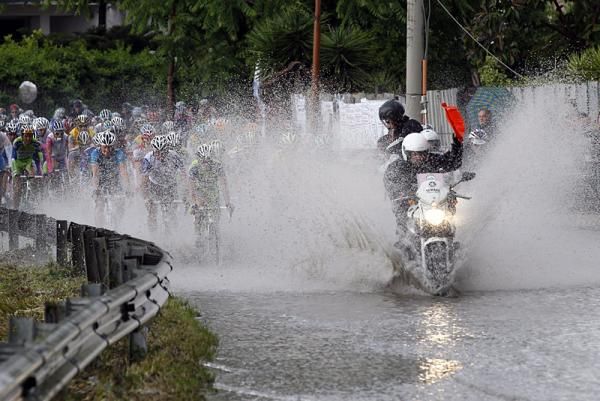 The head of the peloton is further soaked under a wall of water kicked up by a motorcycle.