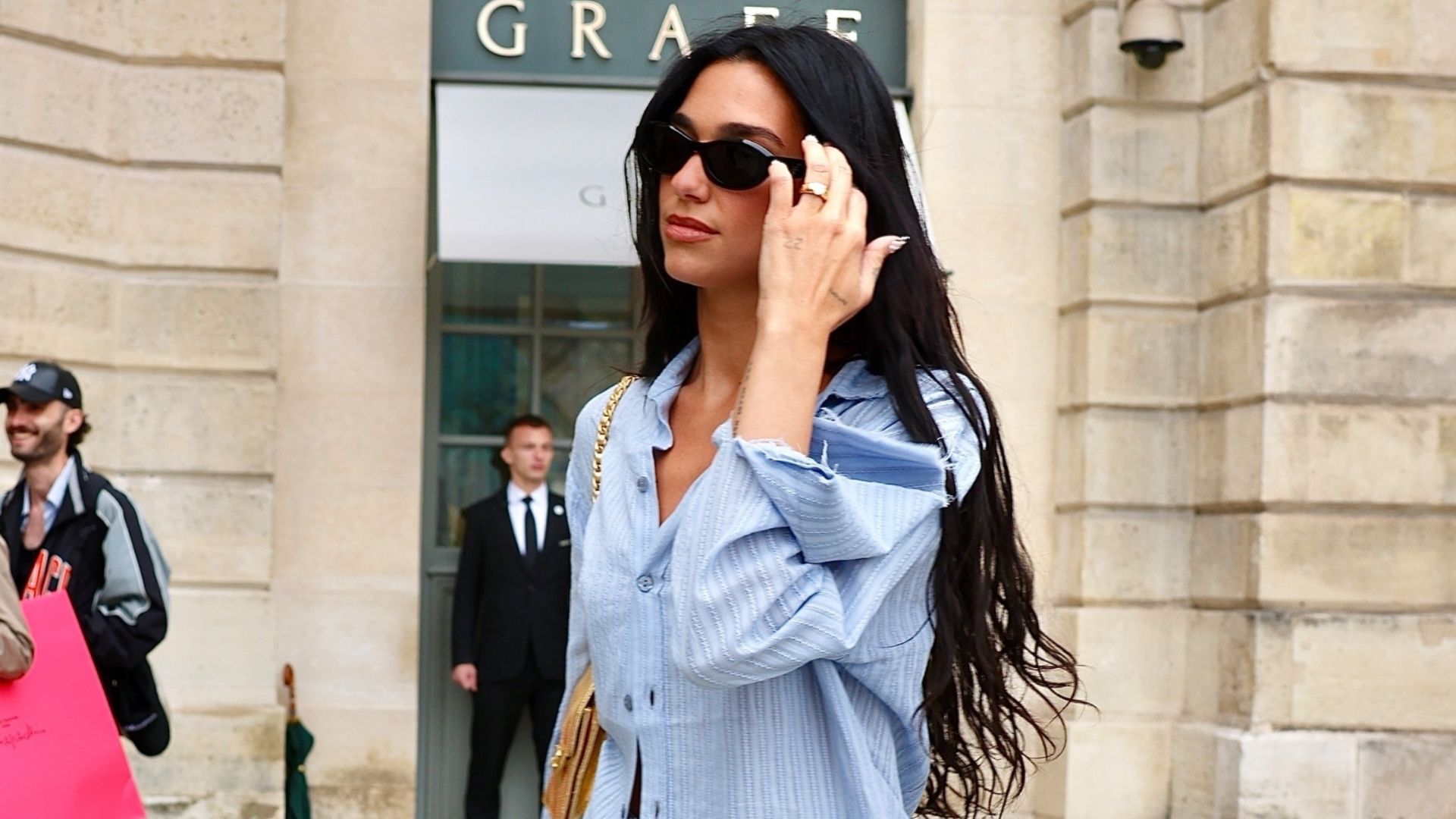 Dua Lipa wears a blue shirt, jeans and peep-toe mules as she walks down the street in Paris.